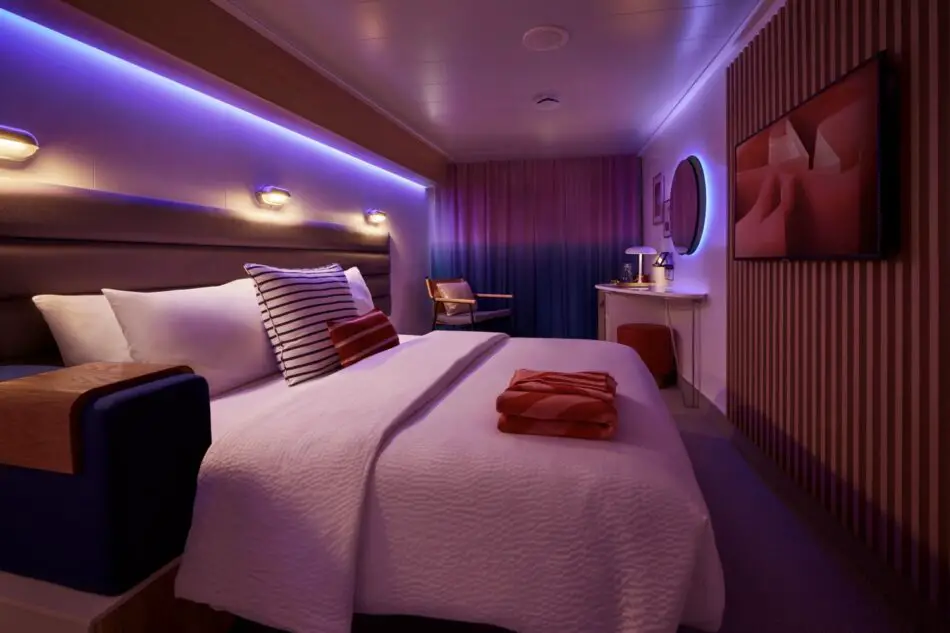 Virgin Voyages cabin on a cruise ship with a large bed and purple mood lighting