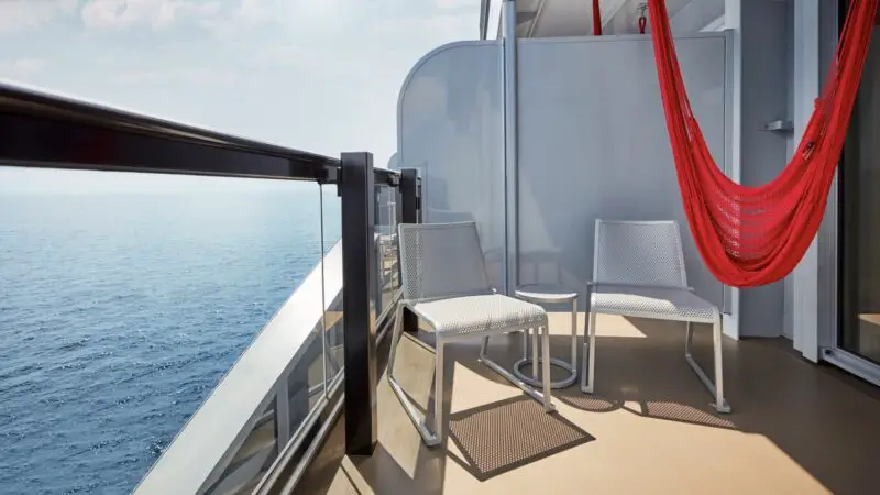 Balcony on a Virgin Voyages cruise ship with a red hammock and two chairs overlooking the ocean