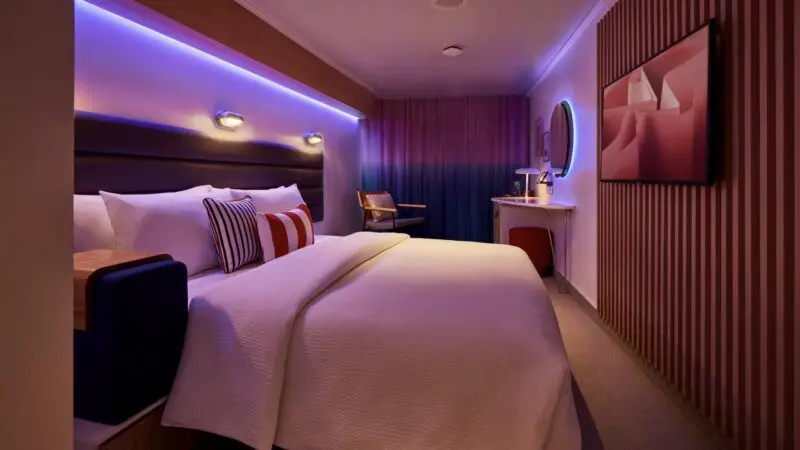 A Virgin Voyages cruise ship cabin with a large bed and purple ambient lighting