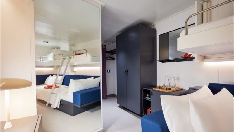 Compact cruise ship cabin with bunk bed, sofa, and wardrobe on a Virgin Voyages cruise ship