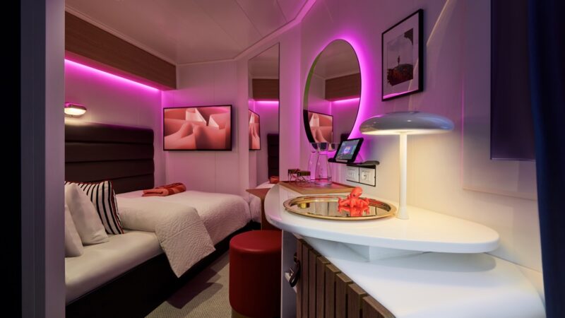 Virgin Voyages cruise ship cabin with pink ambient lighting and twin beds