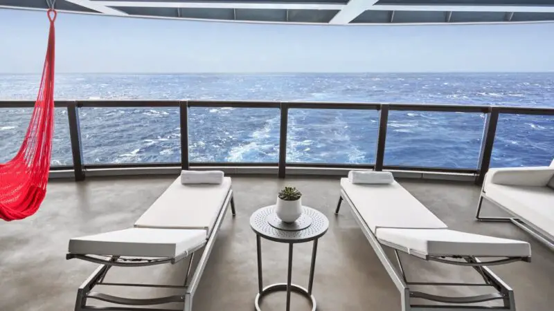 Two lounge chairs on a Virgin Voyages cruise ship balcony with a small table and plant overlooking the ocean