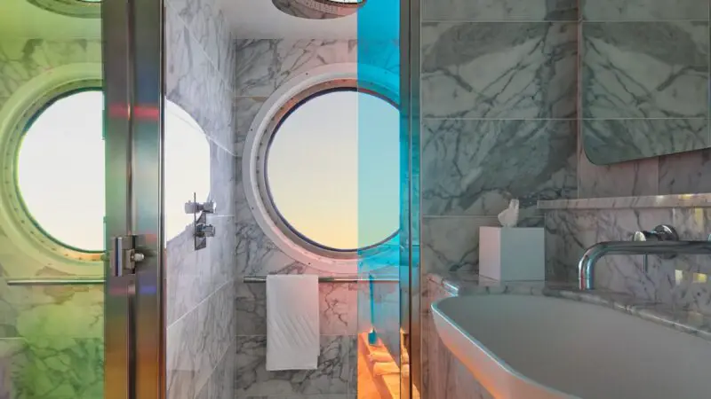 Luxurious marble bathroom with circular porthole on a Virgin Voyages cruise ship