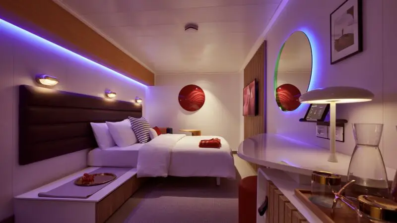 Virgin Voyages cruise ship cabin with large bed and purple lighting