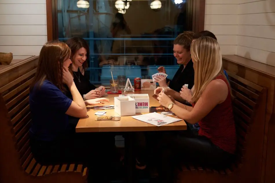 Five women play cards at a restaurant booth