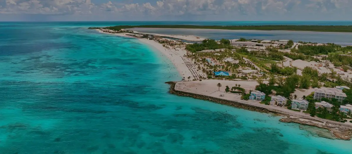 Aerial view of a tropical coastline with turquoise waters and beachfront buildings nestled among greenery.