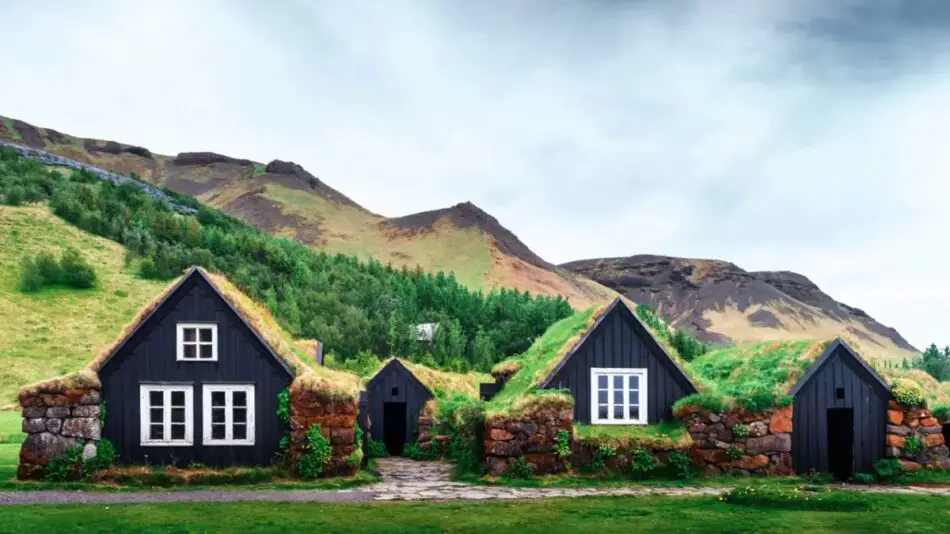 Turf-roofed cottages with black wooden facades against a backdrop of green hills and mountains.