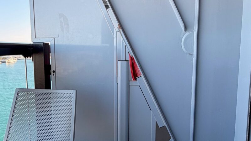 A Virgin Voyages cruise ship balcony with a metal chair and structural elements, offering a view of the ocean.