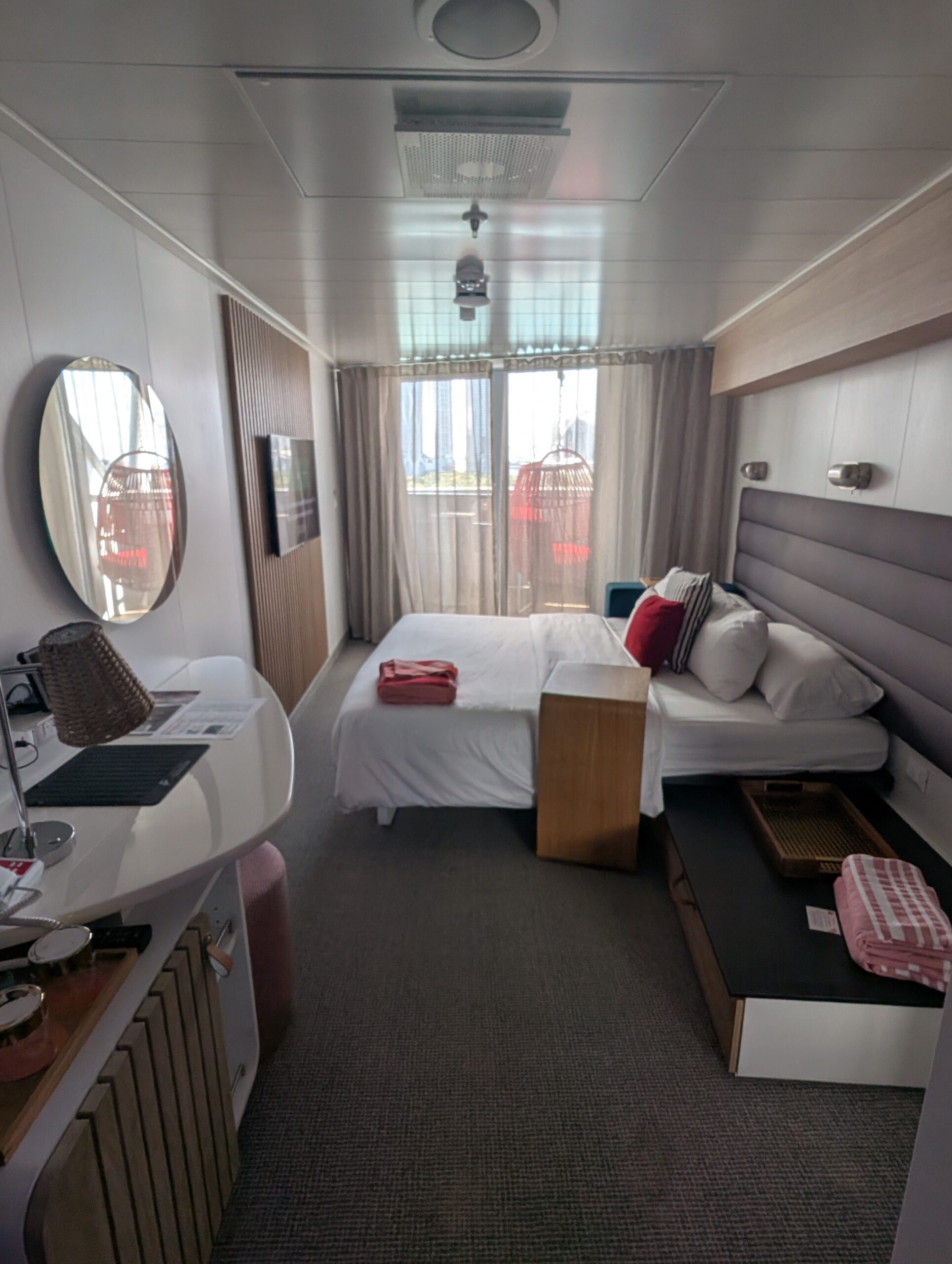 Virgin Voyages cruise ship cabin with modern decor, featuring a bed, circular mirror, and balcony access.