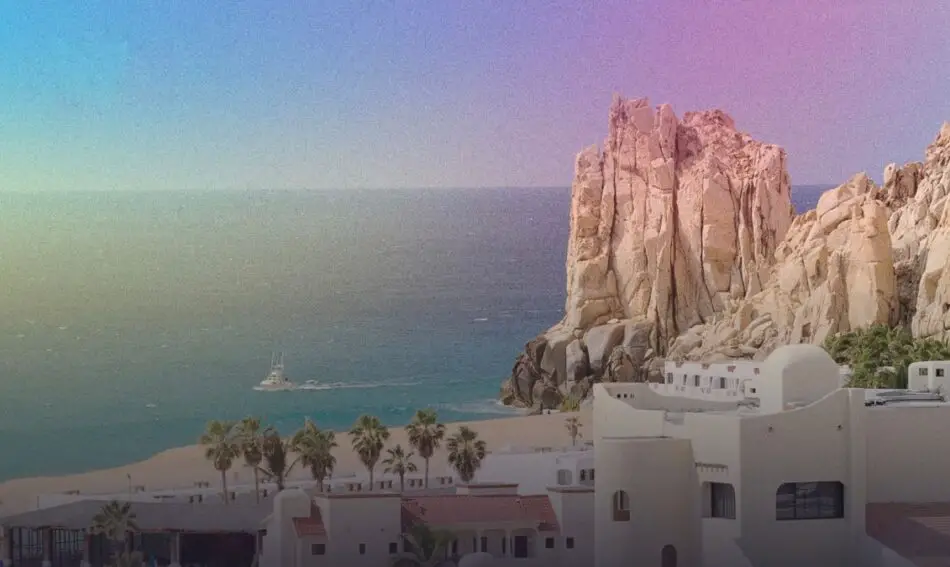 Scenic coastal landscape with large rocky cliffs, palm trees, and a boat on the ocean under a vibrant sky.
