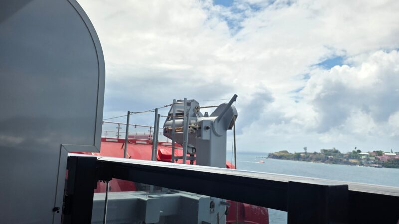 View from a Virgin Voyages cruise ship cabin balcony, showing a lifeboat and ocean under a cloudy sky.
