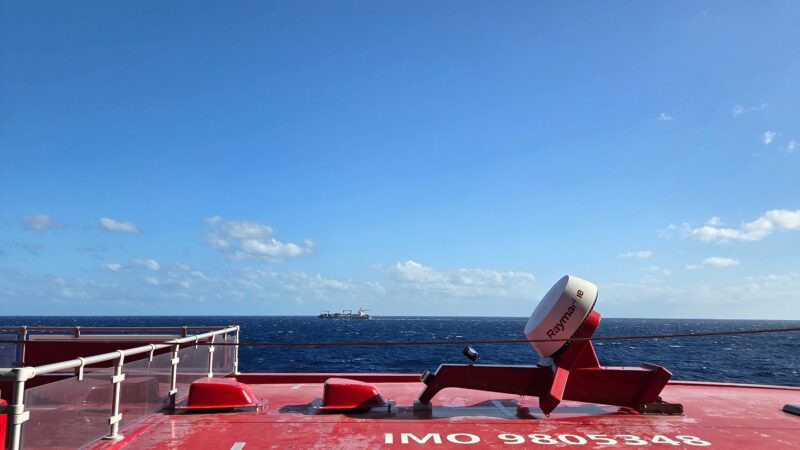 A view from a Virgin Voyages cruise ship deck showing the ocean and a distant ship under a clear blue sky.