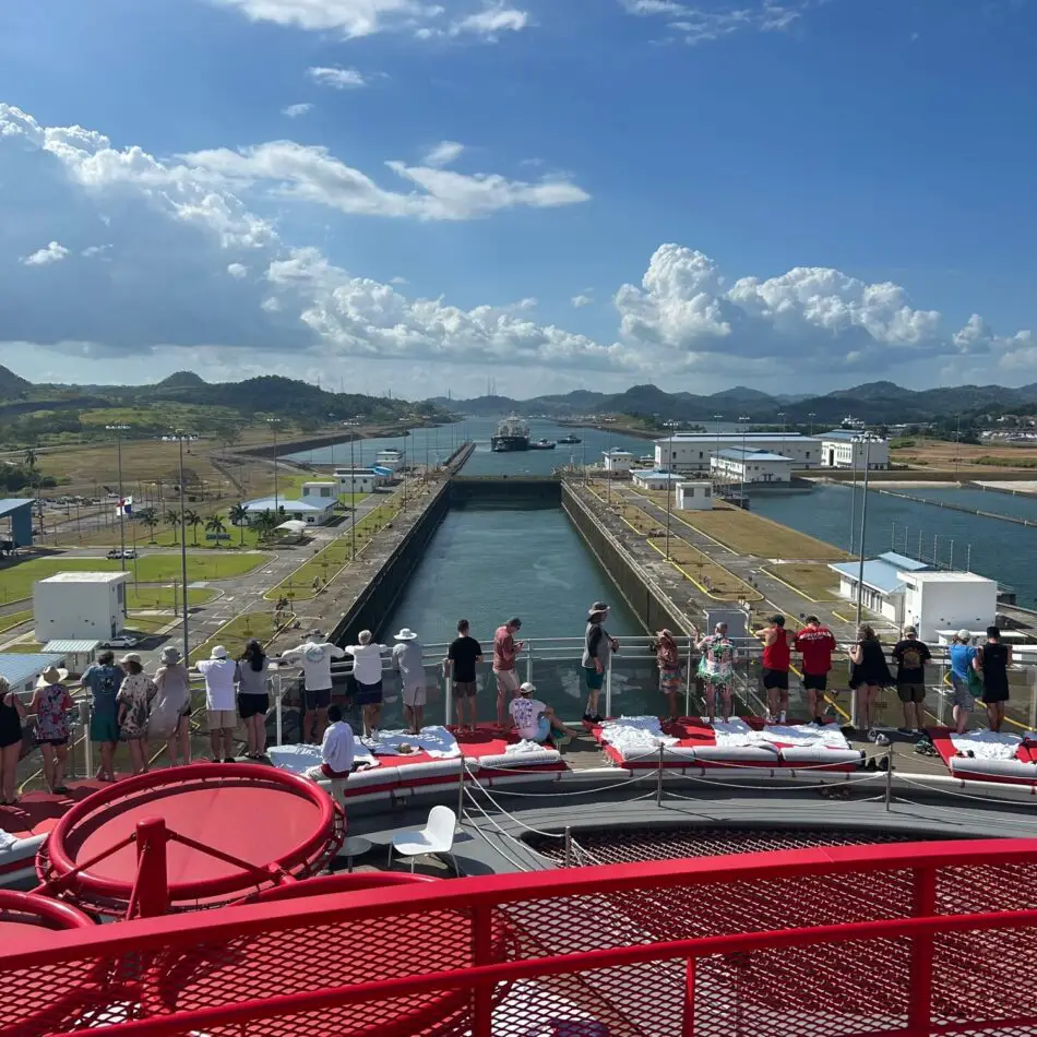 Passengers on a Virgin Voyages ship deck overlooking a canal lock.