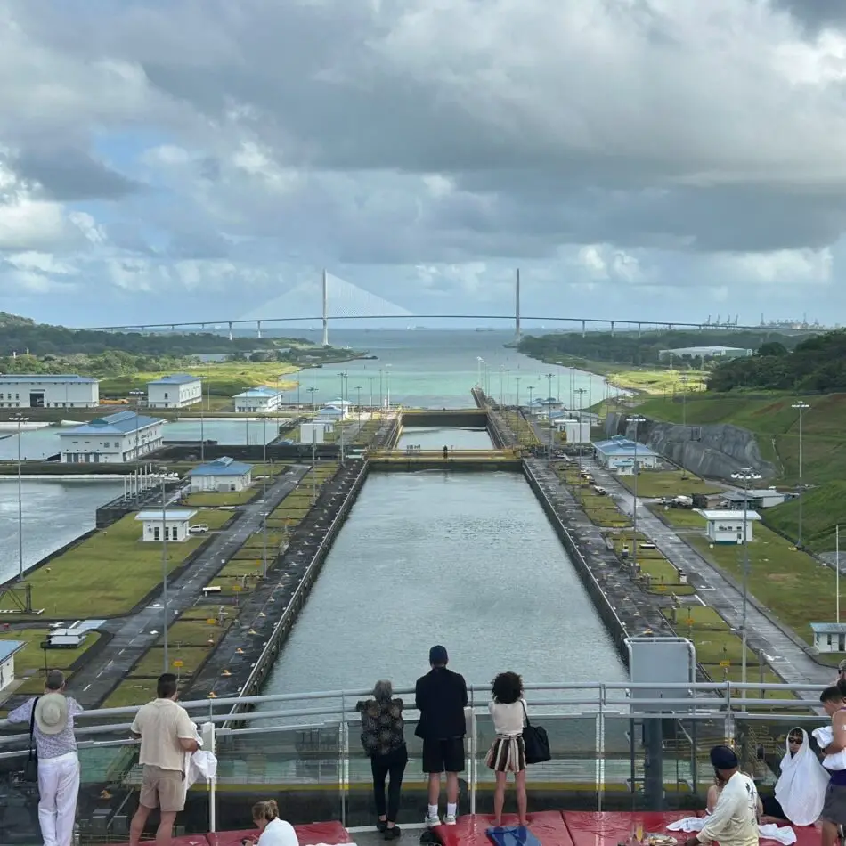 People on a viewing deck overlook a canal lock system and a distant bridge