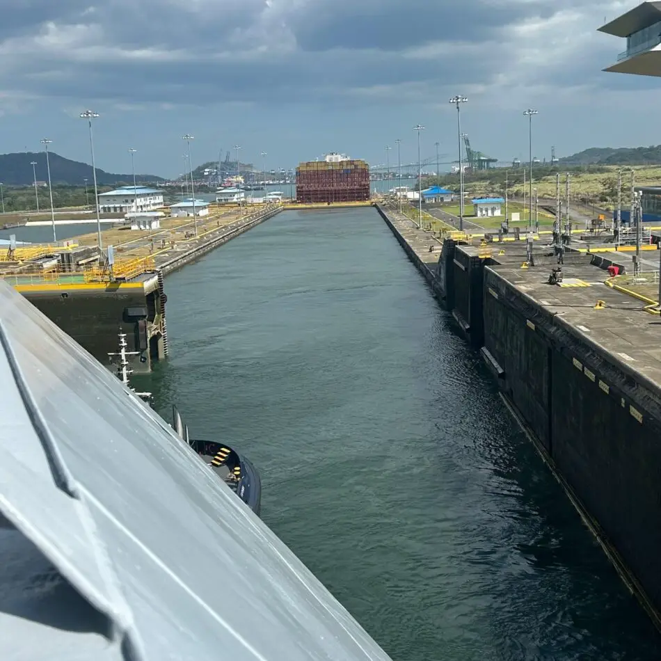 View from a ship's deck into a canal lock with a stacked container ship ahead