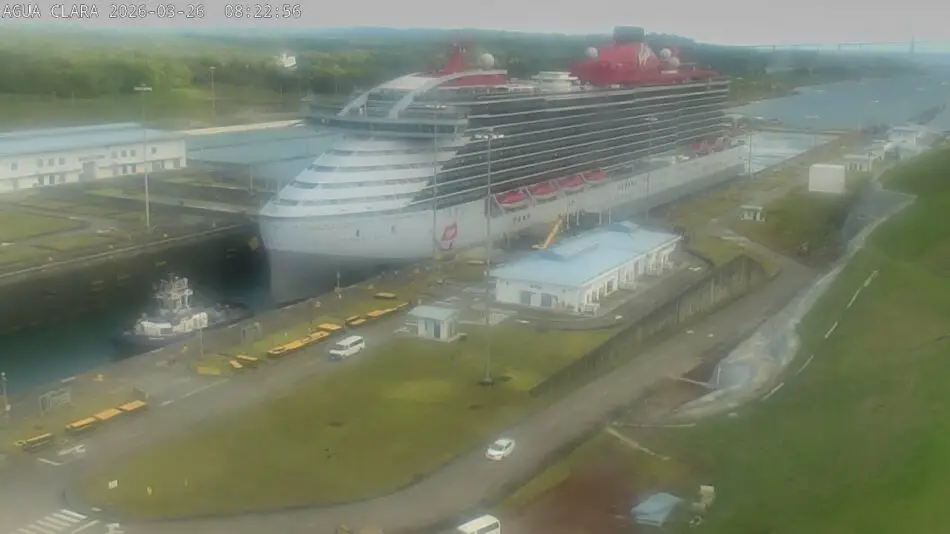 Large cruise ship docked at a canal port with a small tugboat nearby