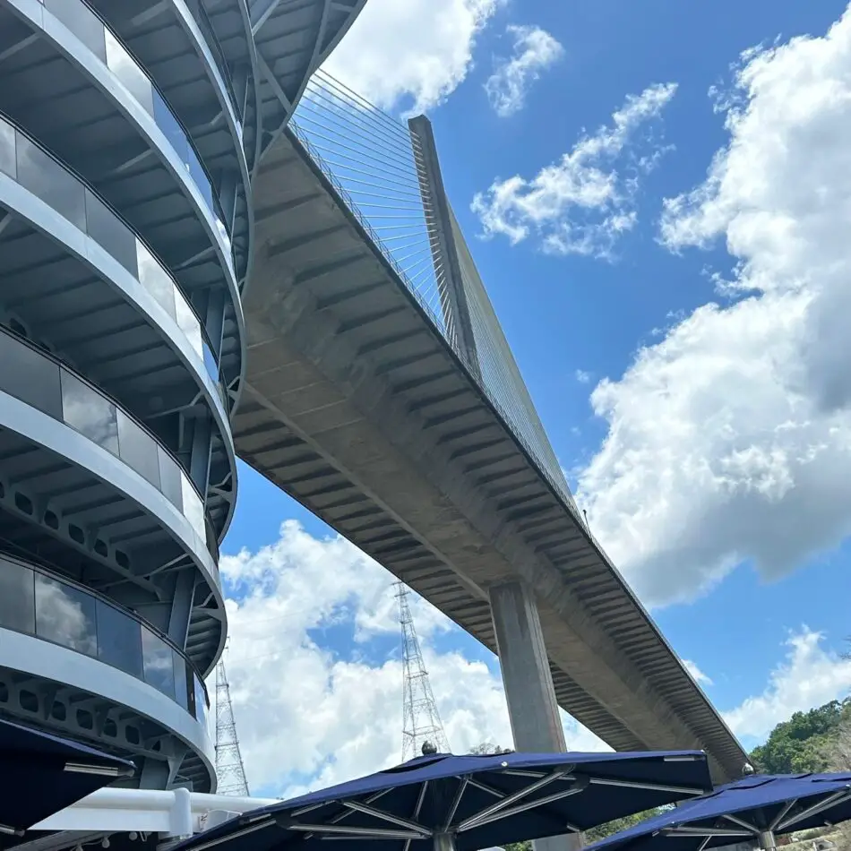 Cable-stayed bridge beside a curved glass-fronted building under a blue sky
