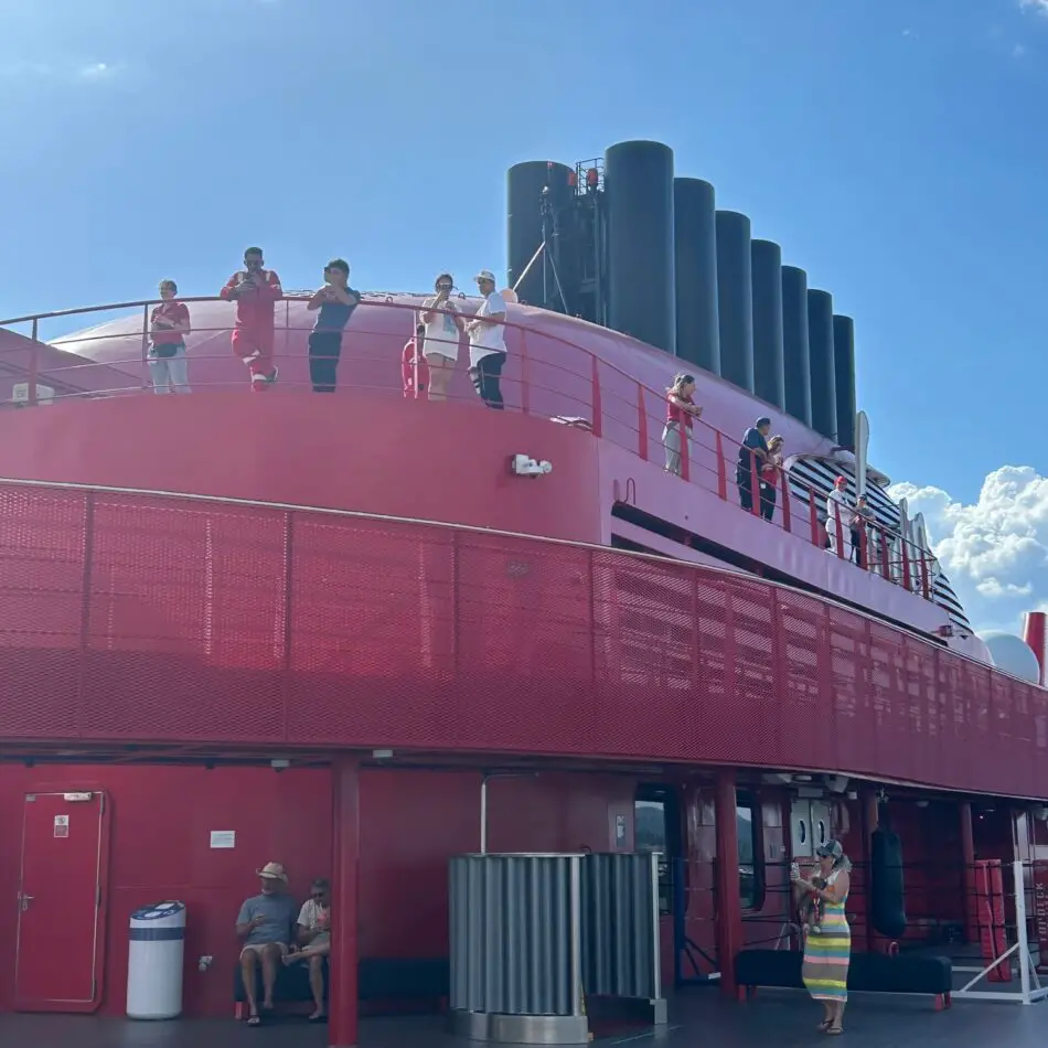 People on the upper deck of a pink Virgin Voyages cruise ship