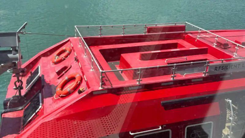 View from a Virgin Voyages cruise ship cabin, showing a red lifeboat and city skyline through the window.