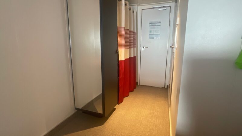 Virgin Voyages cruise ship cabin hallway featuring a mirror, red and white striped curtains, and a closed door.
