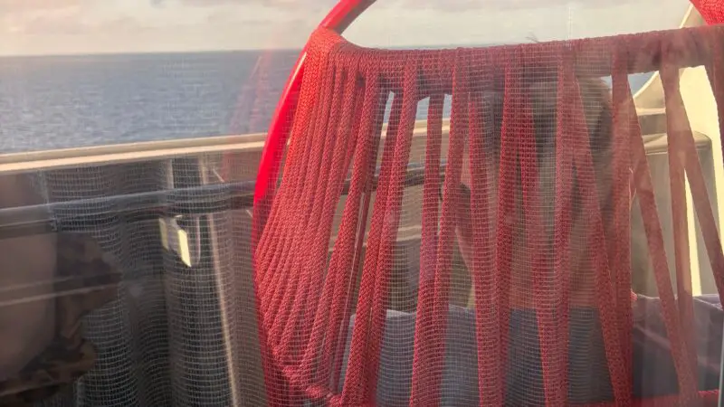 Balcony of a Virgin Voyages cruise ship cabin with a red hanging chair and ocean view.