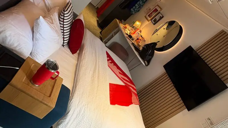 Virgin Voyages cruise ship cabin with a bed, wall-mounted TV, and a desk with a round mirror.