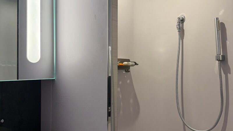 Bathroom of a Virgin Voyages cruise ship cabin featuring a modern sink, illuminated mirror, and a shower with a rainfall showerhead.