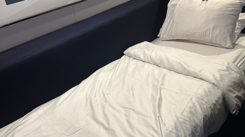 Virgin Voyages cruise ship cabin interior showing a bed with white linens, a couch, colorful pillows, and a modern art piece above.