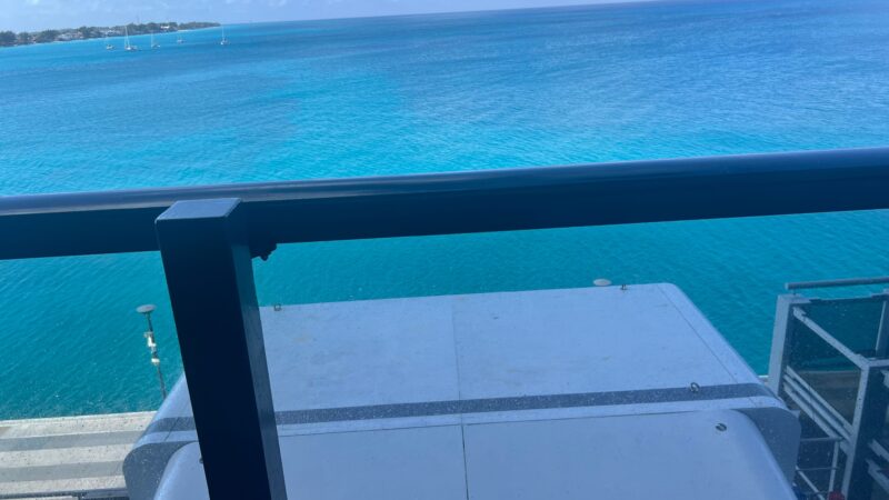 View from a Virgin Voyages cruise ship balcony cabin overlooking the ocean, with a railing and clear blue water in the background.