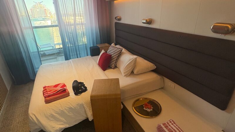 Virgin Voyages cruise ship cabin with a double bed, modern furnishings, and a balcony view.