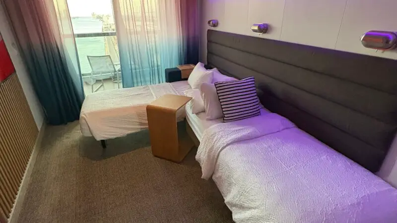Virgin Voyages cruise ship cabin with twin beds, a large window, and balcony view.