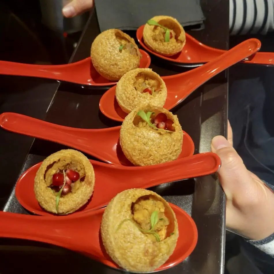 Crispy hollow croquettes filled with savory filling on bright red spoons