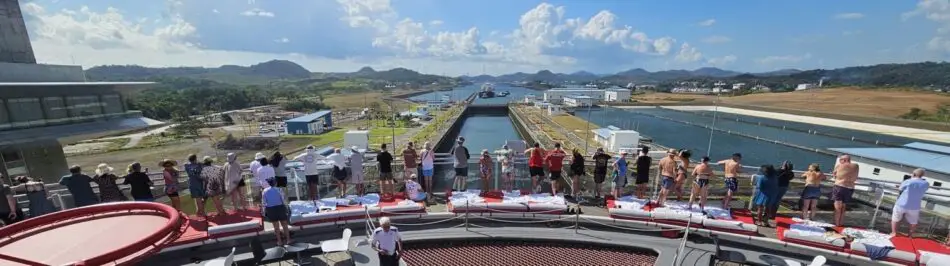 Passengers on a cruise ship upper deck overlooking a canal and hills