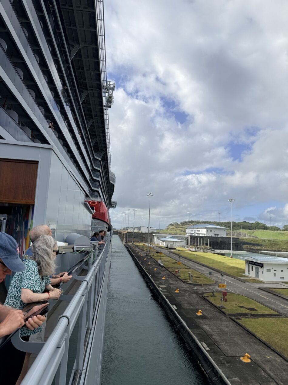 Passengers on a Virgin Voyages cruise ship deck overlooking a dock
