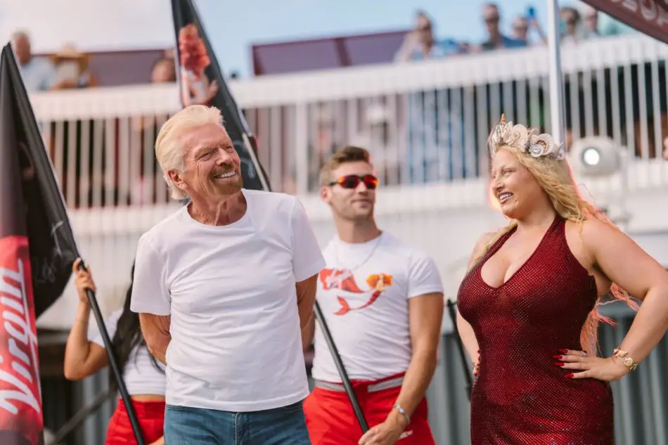 Smiling man in white T-shirt and woman in sparkling red dress on a Virgin Voyages cruise ship deck