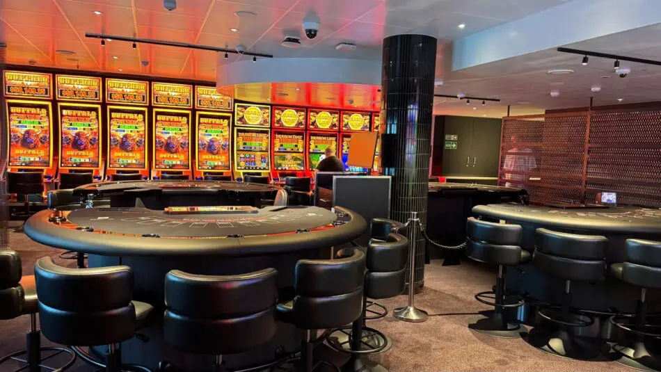 Casino floor on a Virgin Voyages cruise ship with slot machines and round blackjack tables