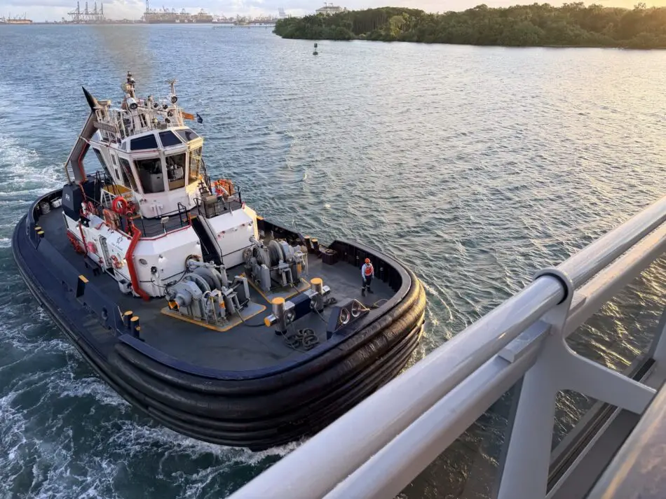 Harbor tugboat beside a large cruise ship, with port cranes in the distance