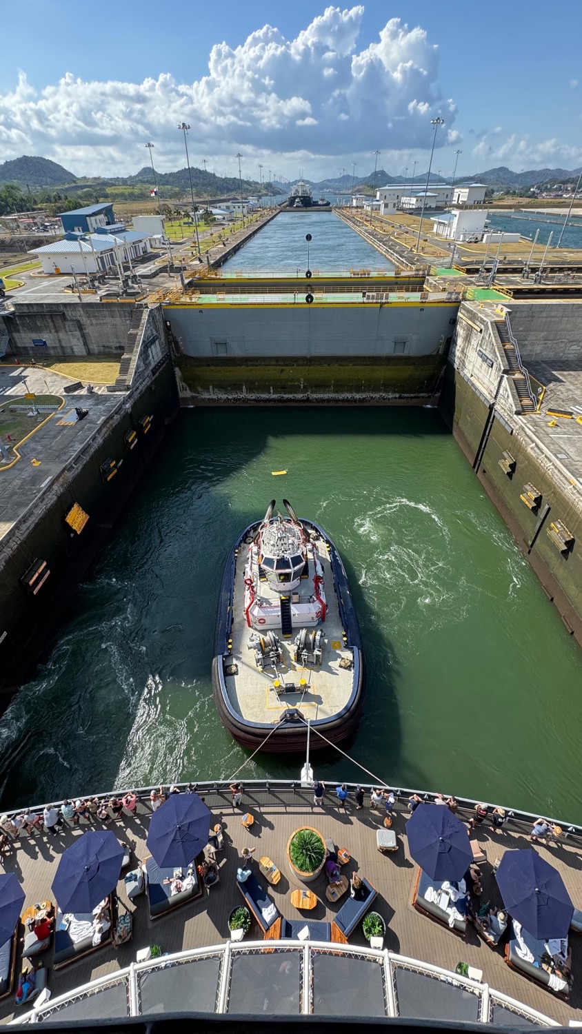 Cruise ship deck with blue umbrellas overlooks a canal lock with a tugboat