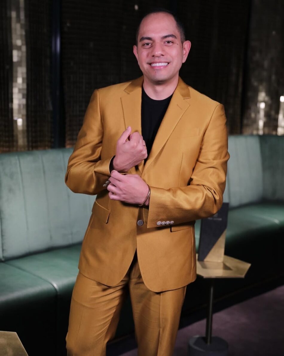 Smiling man in a gold suit adjusting his jacket sleeve in a lounge