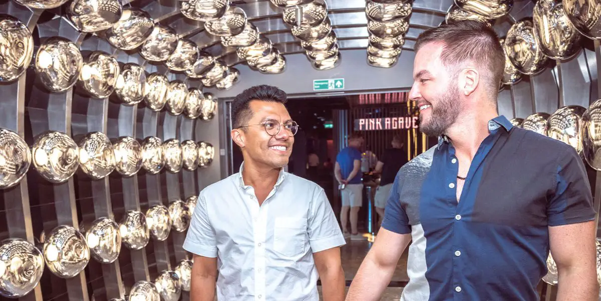 Two people walking and smiling in a corridor with reflective metallic wall fixtures.