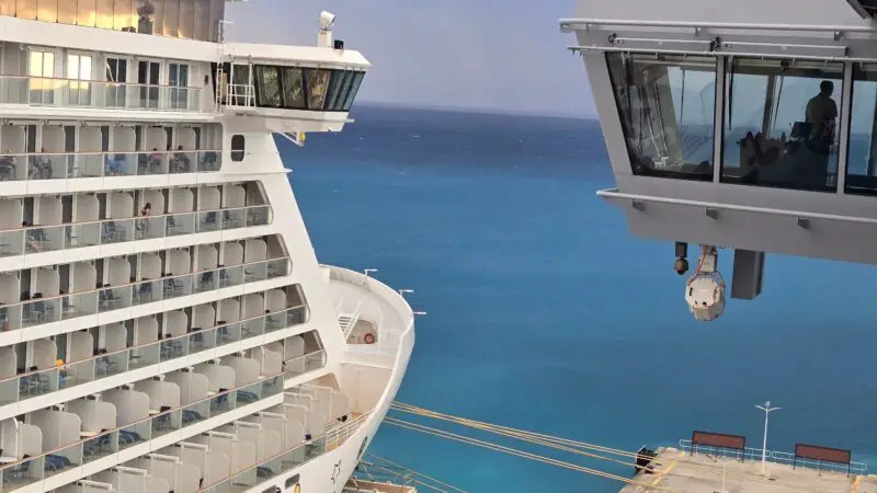 View from a Virgin Voyages cruise ship cabin balcony overlooking a dock and the ocean with another ship nearby.