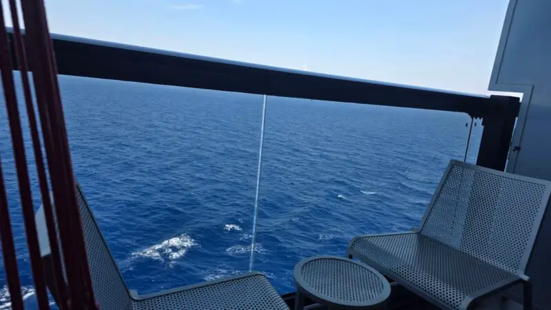 Balcony of a Virgin Voyages cruise ship cabin with two chairs, a small table, and an ocean view.