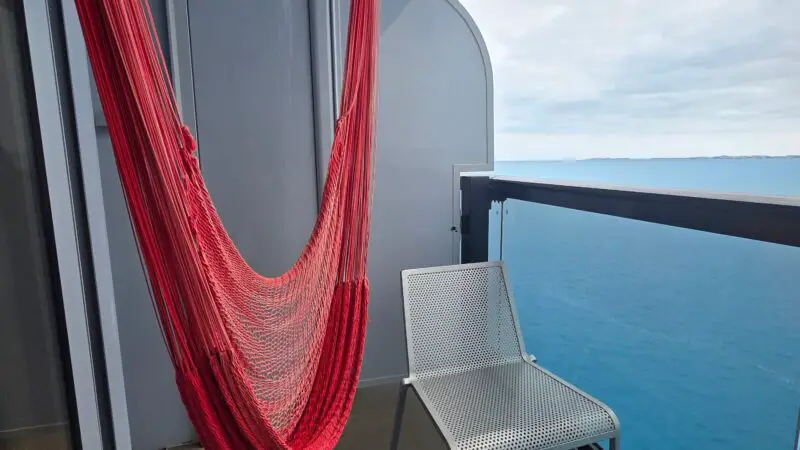 Virgin Voyages cruise ship balcony featuring a red hammock, white chair, and circular table, overlooking the ocean.