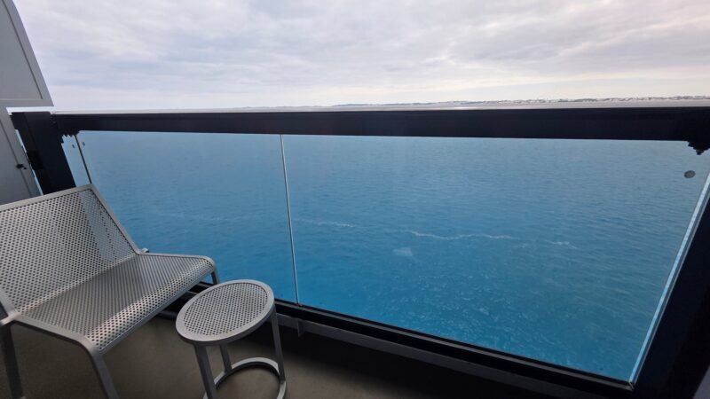 Balcony of a Virgin Voyages cruise ship cabin with a metal chair and small table, overlooking the sea.