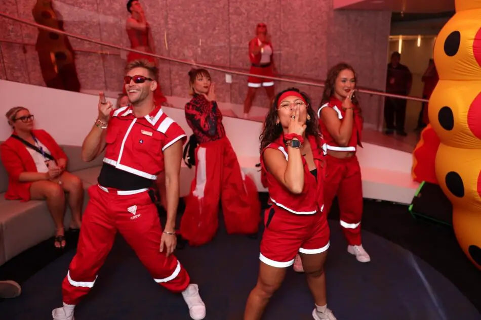 Virgin Voyages crew dancing in red uniforms aboard a ship lounge