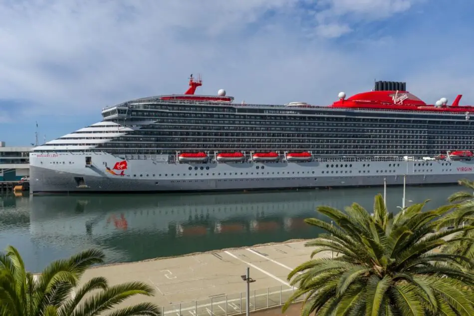 Virgin Voyages cruise ship docked at a port with palm trees in the foreground