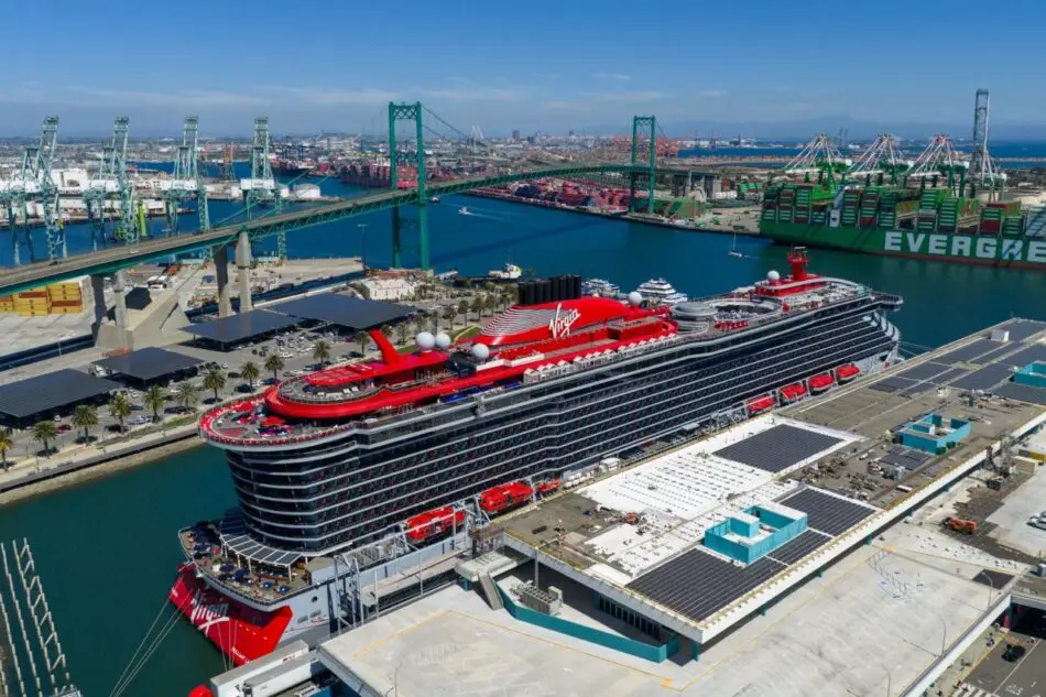 Virgin Voyages cruise ship docked at a busy harbor with cranes