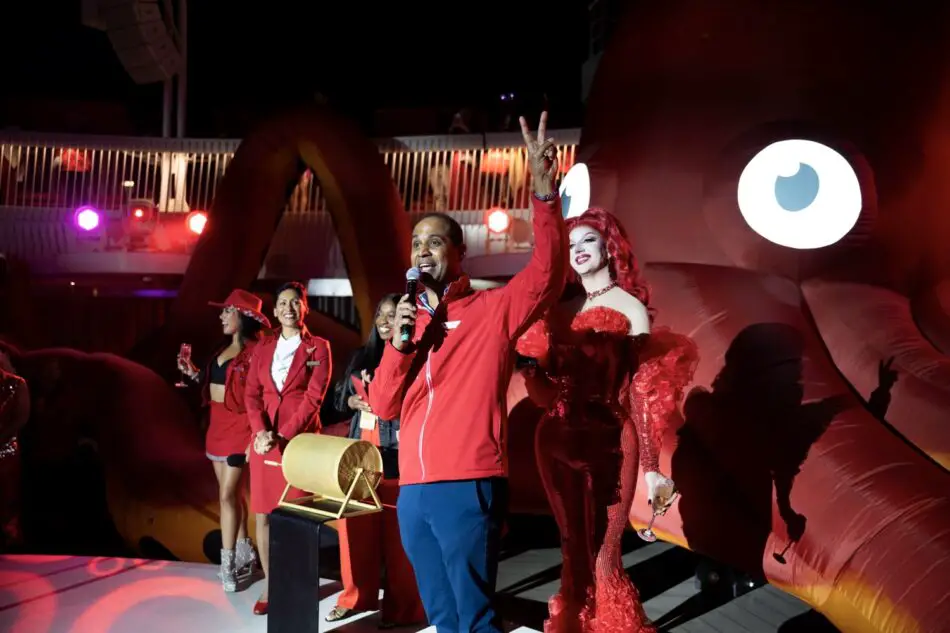 Host speaks into a microphone on stage aboard a Virgin Voyages cruise ship