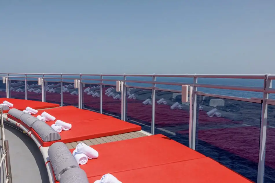 Red cushioned lounge chairs on a cruise ship deck overlooking the ocean
