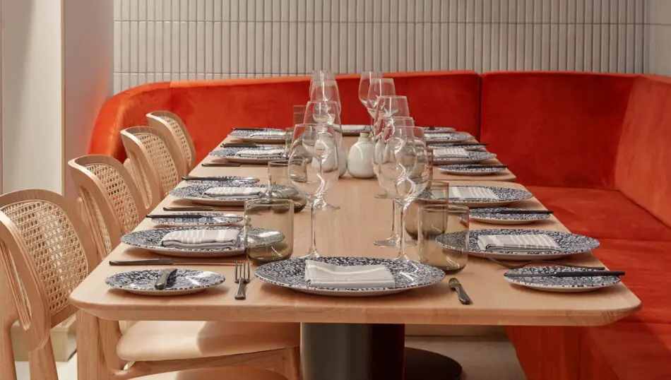 Long wooden dining table set for a group with blue patterned plates and glassware on a Virgin Voyages cruise ship